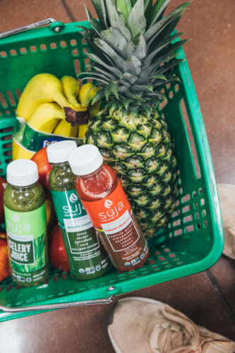 Three Suja bottles in a shopping basket with fruit
