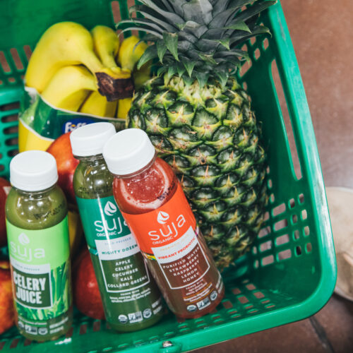 Three Suja bottles in a shopping basket with fruit